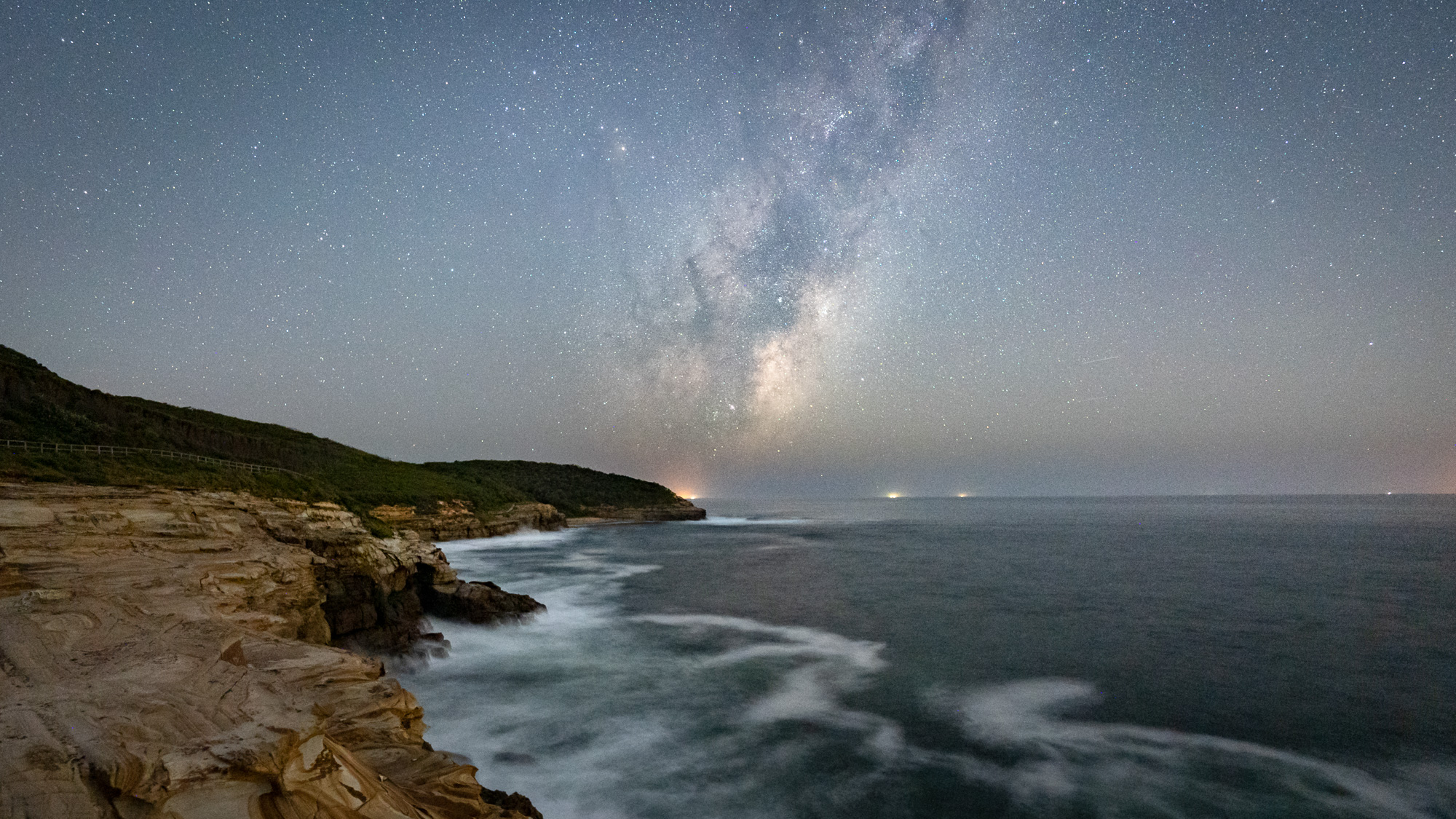 The Milky Way rises above the coast while taking in the patterned sandstone cliffs of Bouddi National Park on the Central Coast, New South Wales, Australia